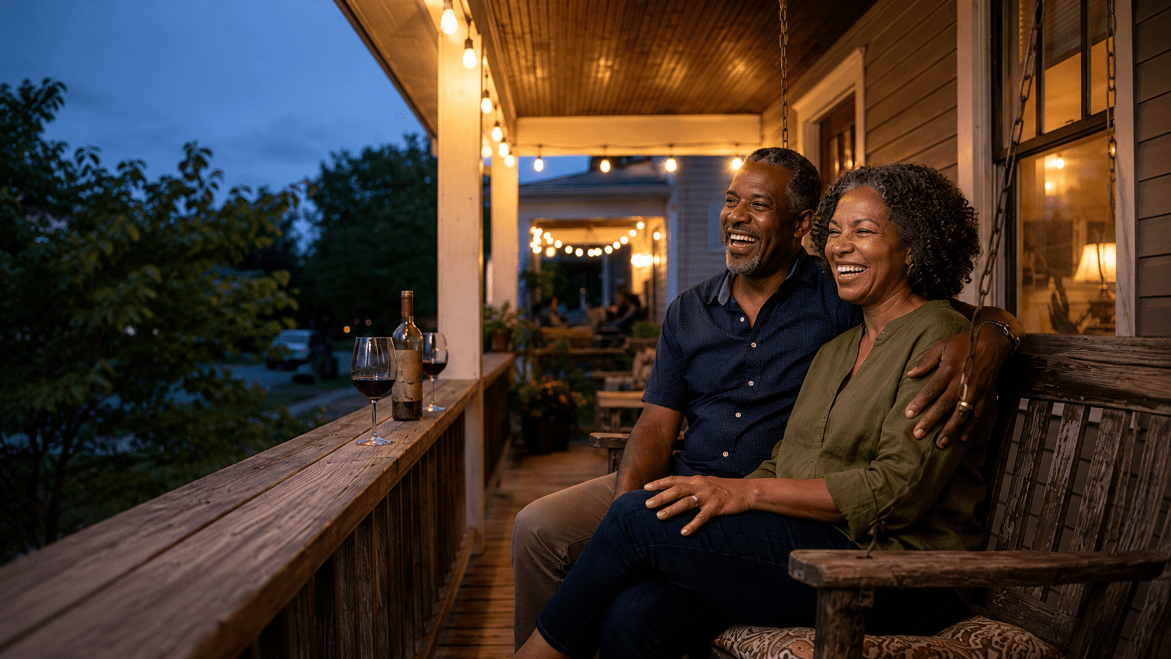 Couple laughing together on a porch swing under string lights at dusk